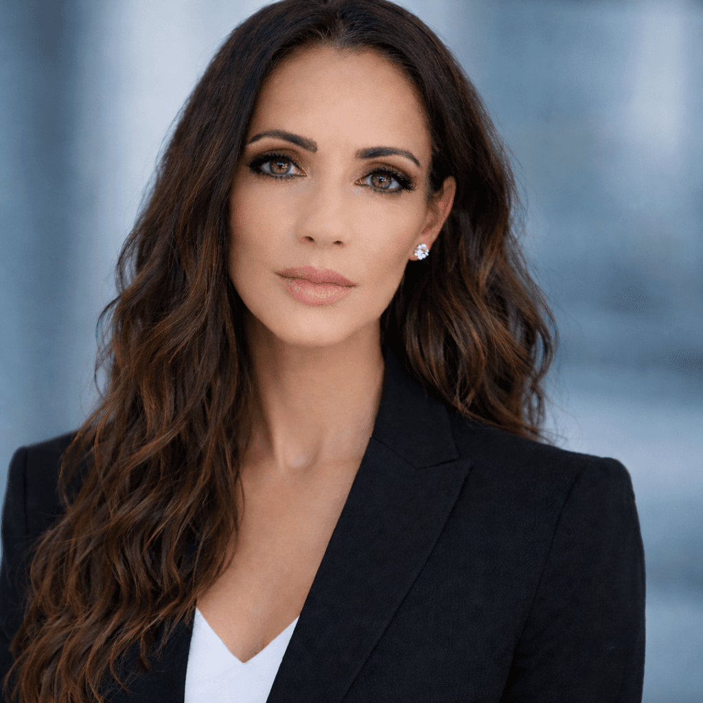 Woman with long wavy brown hair and green eyes wearing a tailored black blazer.