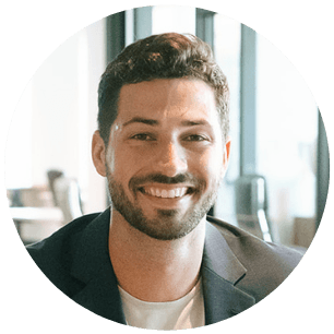 Smiling man with a beard wearing a blazer in a bright, modern office setting.