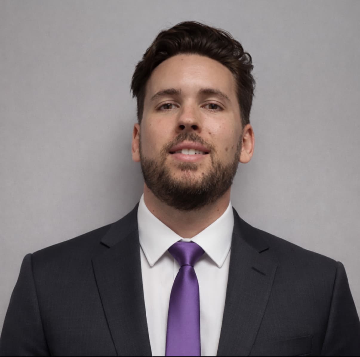 Professional headshot of a bearded man in a dark suit, white shirt, and purple tie.
