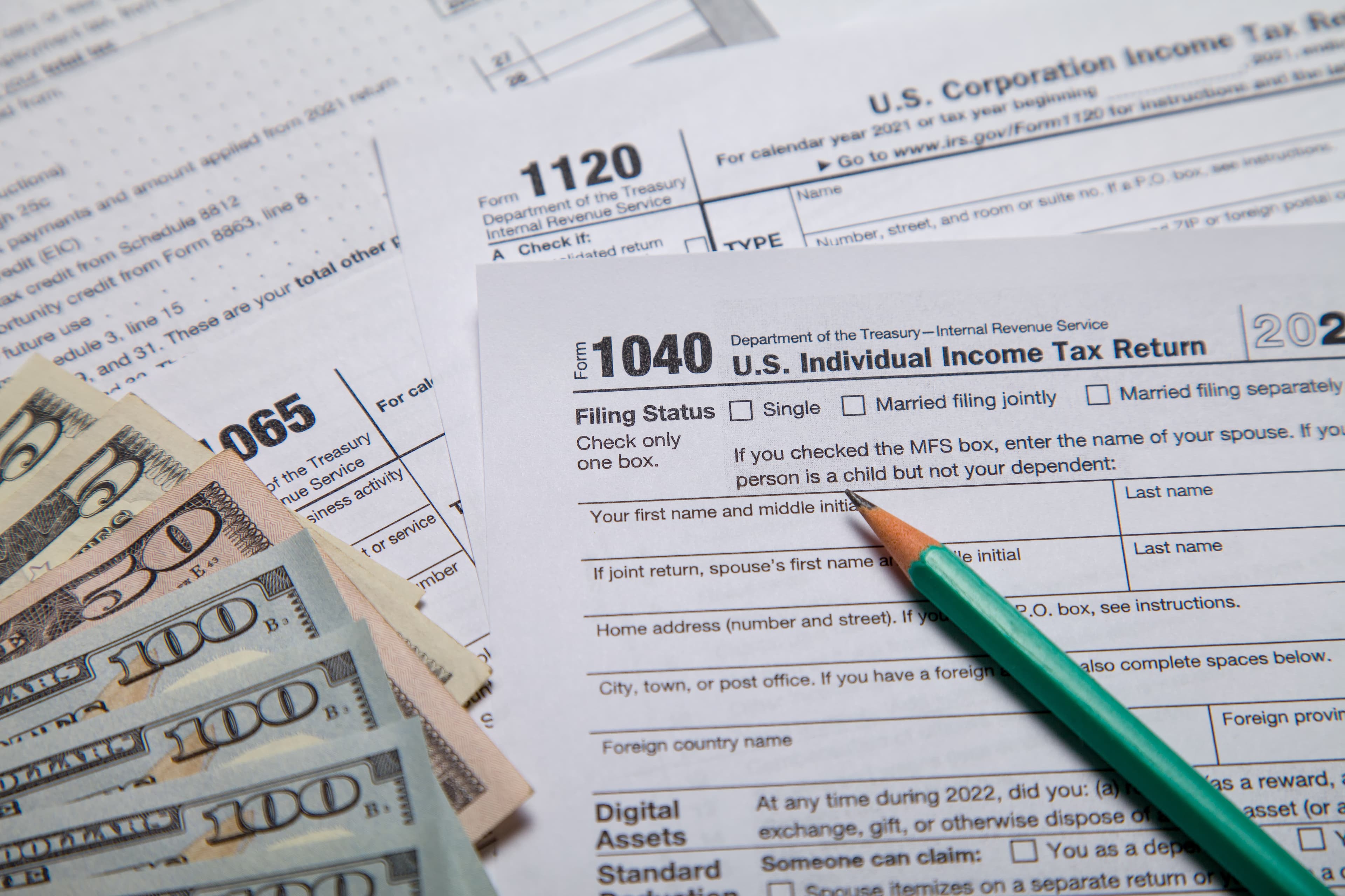 US tax forms including Form 1040 with a green pencil and a fan of cash.